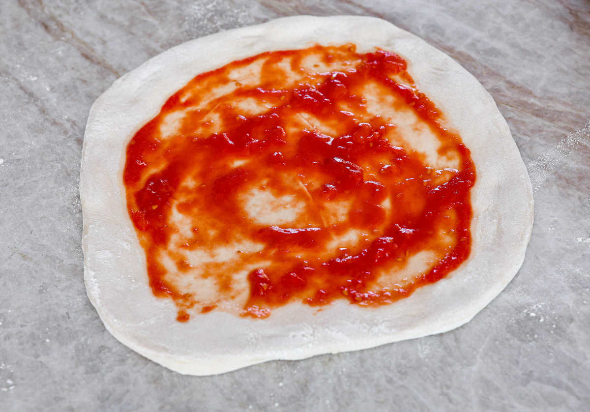This is the perfect beginner's guide for making wood-fired pizza dough! Pizza expert, Chef Brandon Price, taught me how to make authentic homemade pizza, and now you get to learn too! Third photo of the sauce spread on the pizza dough.