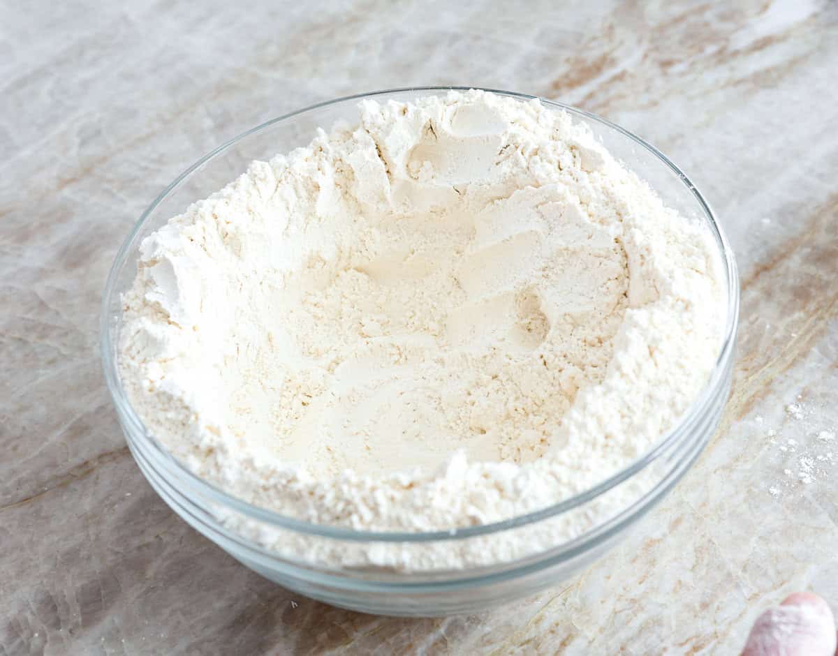 This is the perfect beginner's guide for making wood-fired pizza dough! Pizza expert, Chef Brandon Price, taught me how to make authentic homemade pizza, and now you get to learn too! Second photo of the flour, salt, and yeast in a bowl shaped into a well.