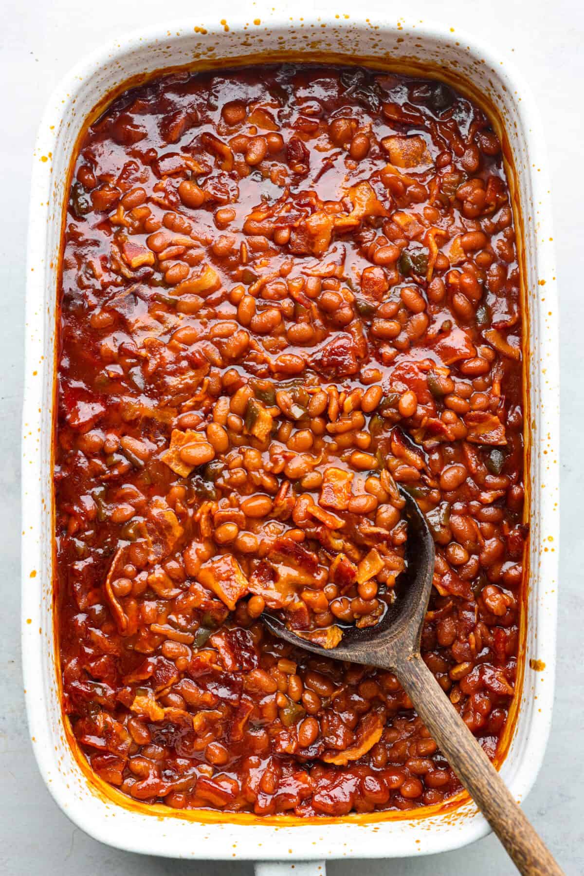 Top view of the world's best baked beans in a baking dish with a wood spoon.