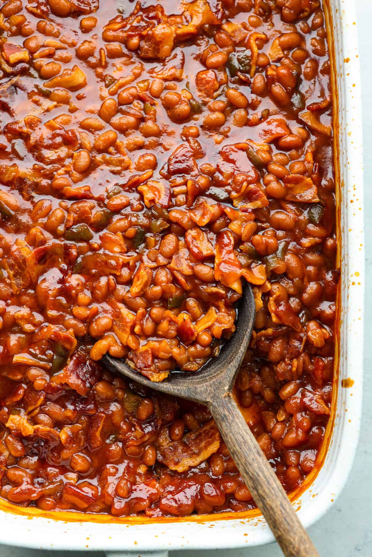Close view of the baked beans in a baking dish with a wooden spoon.