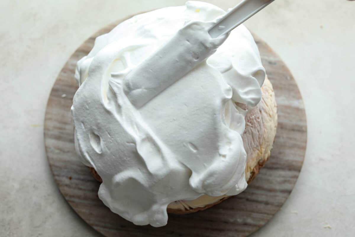 Overhead shot of meringue being spread over ice cream and cake of baked Alaska. 