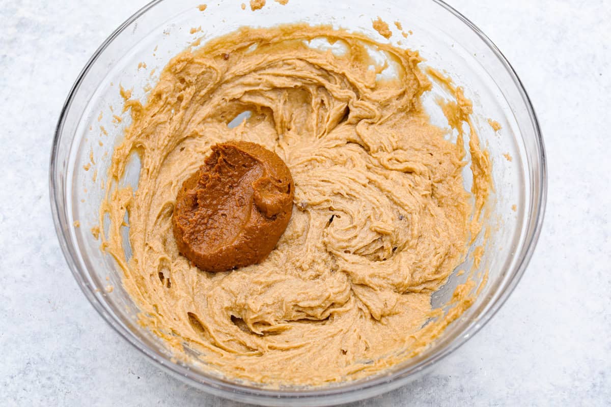 Satisfy your sweet tooth with loaded Biscoff Cookies. They are soft and chewy and infused with the flavor of Biscoff cookies and cookie butter. These are easy to whip up and will be a hit for any occasion! Overhead shot of a bowl of cookie dough with dollop of cookie butter on top.