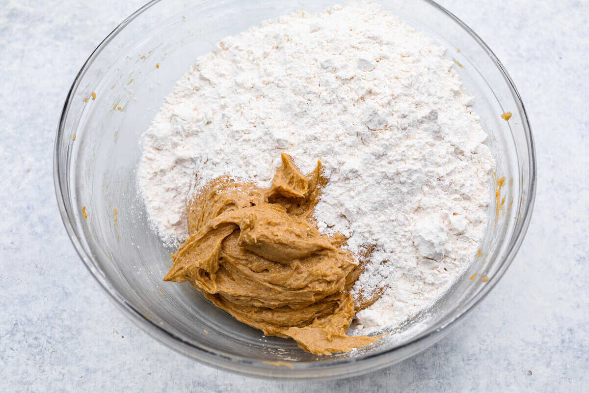 Satisfy your sweet tooth with loaded Biscoff Cookies. They are soft and chewy and infused with the flavor of Biscoff cookies and cookie butter. These are easy to whip up and will be a hit for any occasion! Overhead shot of bowl of cookie dough with dry ingredients on top.