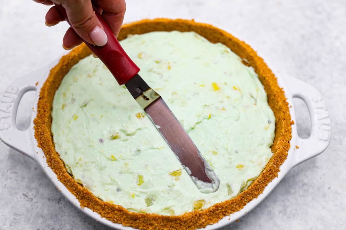 Third photo of a small spatula smoothing the top of the no-bake pistachio cream pie.