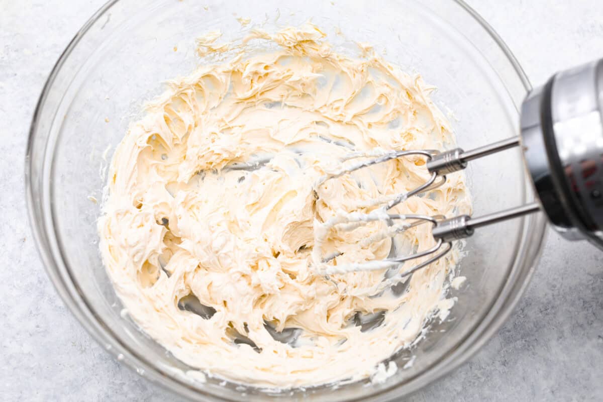Overhead shot of electric mixer mixing cream cheese in a glass bowl.