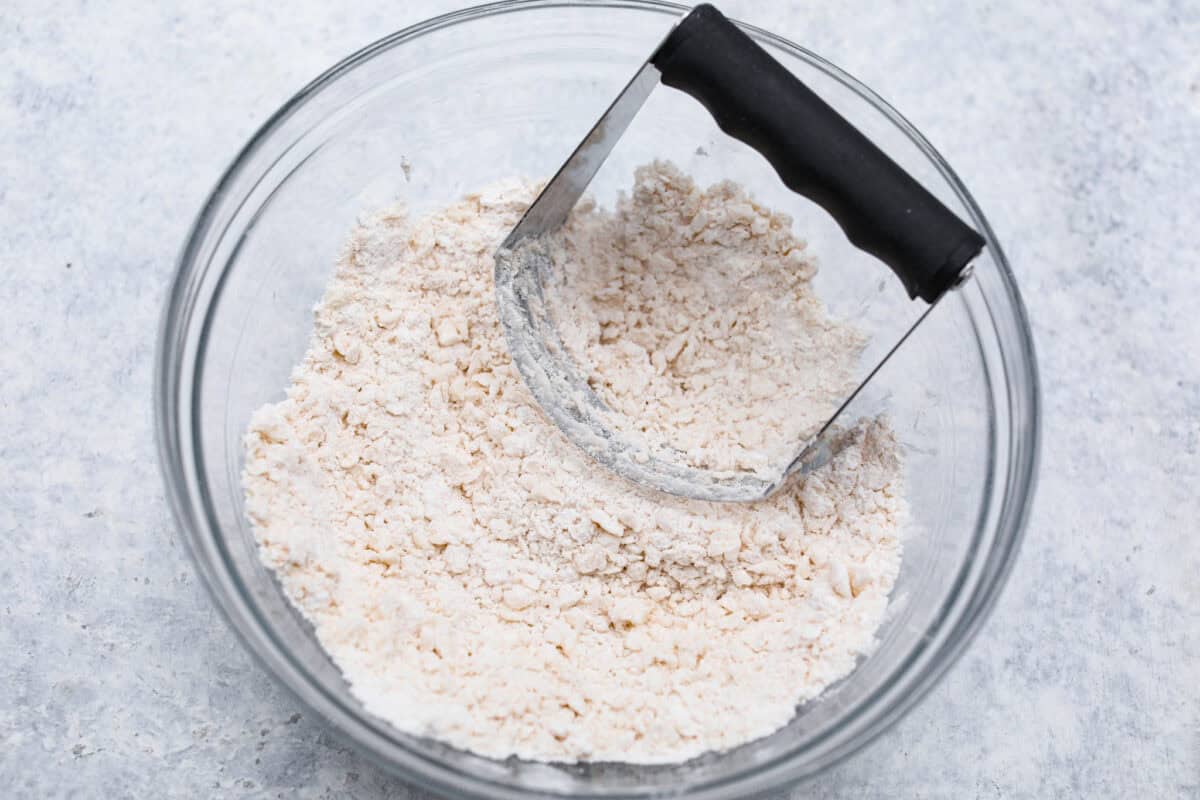 Overhead shot of crust ingredients in glass bowl with pastry cutter. 