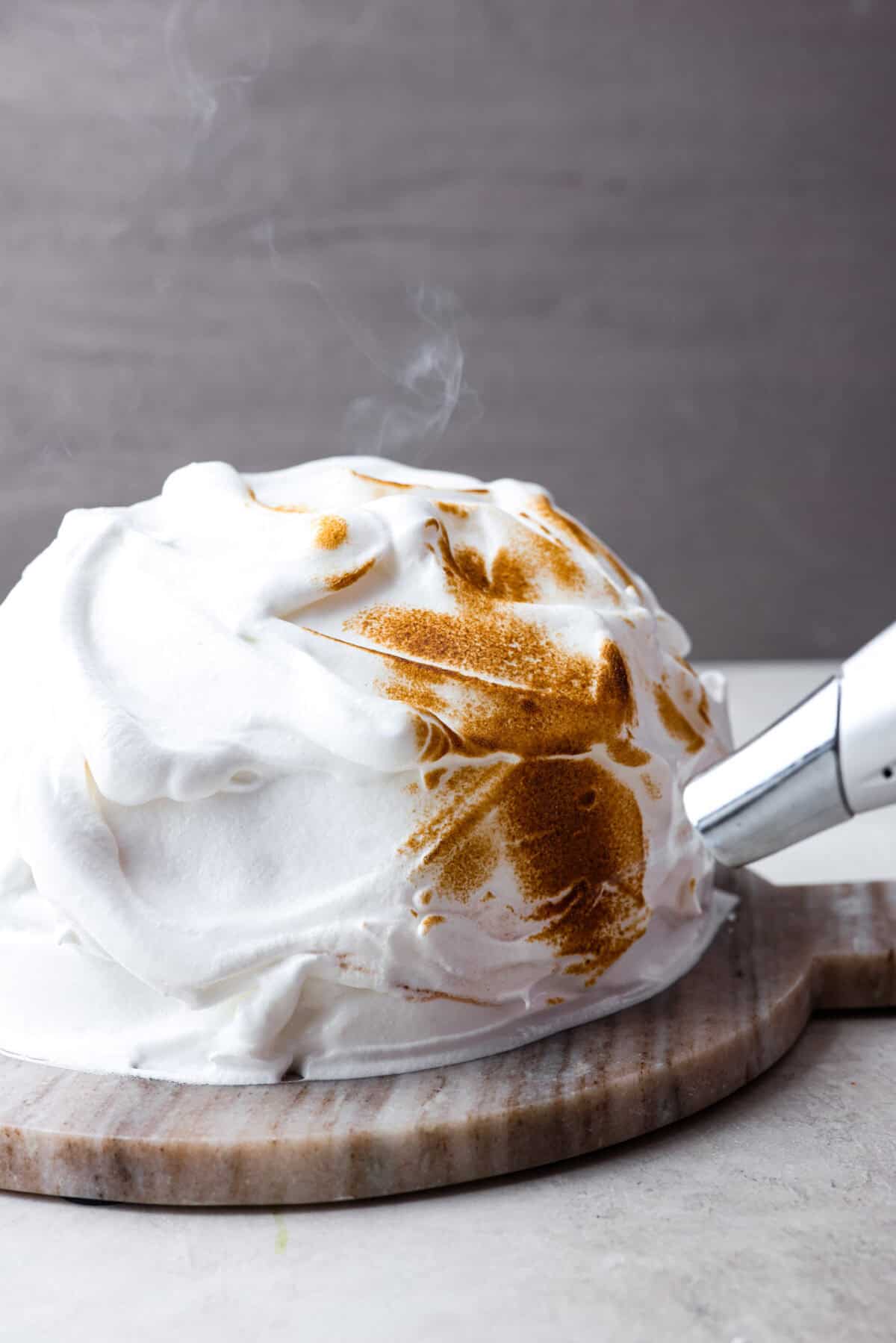 Side shot of baked Alaska covered in meringue being browned with a hand torch. 