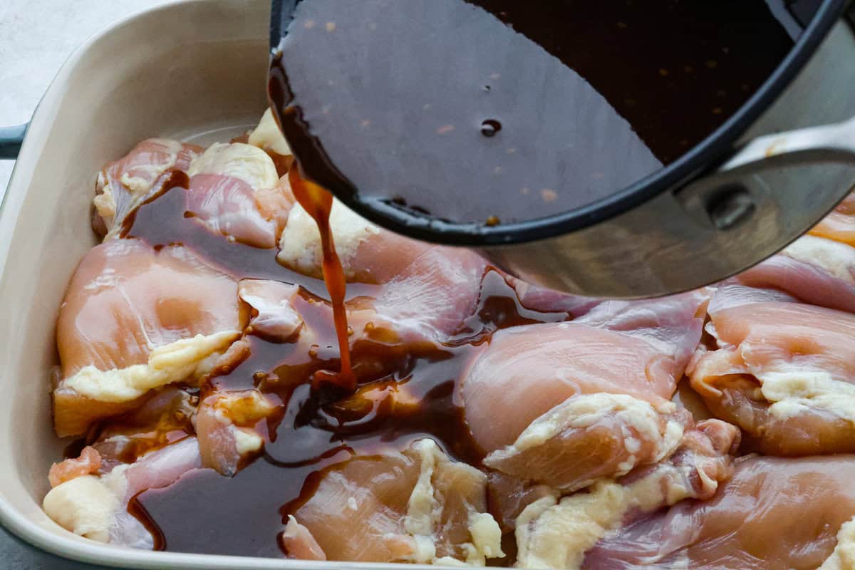 Baked Huli Huli chicken is a tried and true recipe now made in the oven! Tender chicken baked in a sweet and savory sauce. This easy one-pan dinner is full of Hawaiian-inspired flavors! Third photo of the sauce pouring over the chicken.