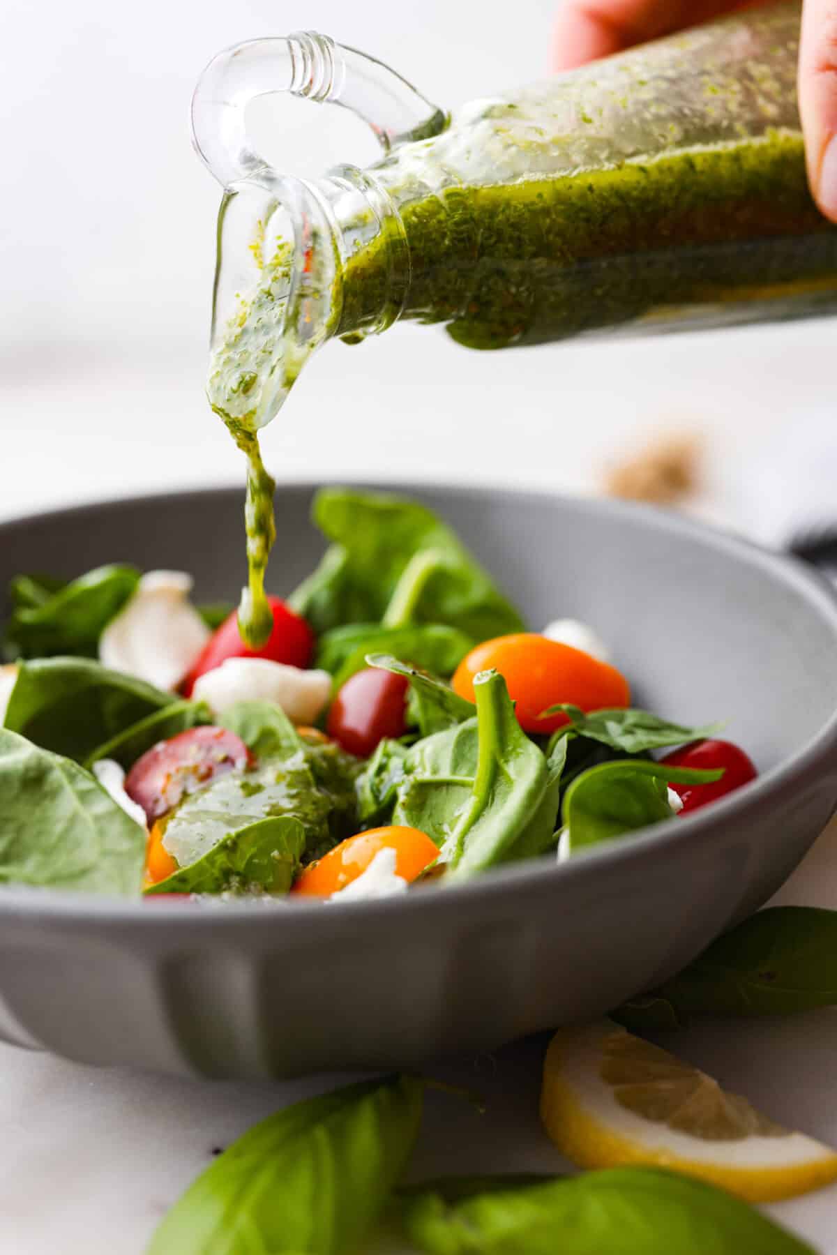 Side shot of basil vinaigrette being poured over a green salad. 