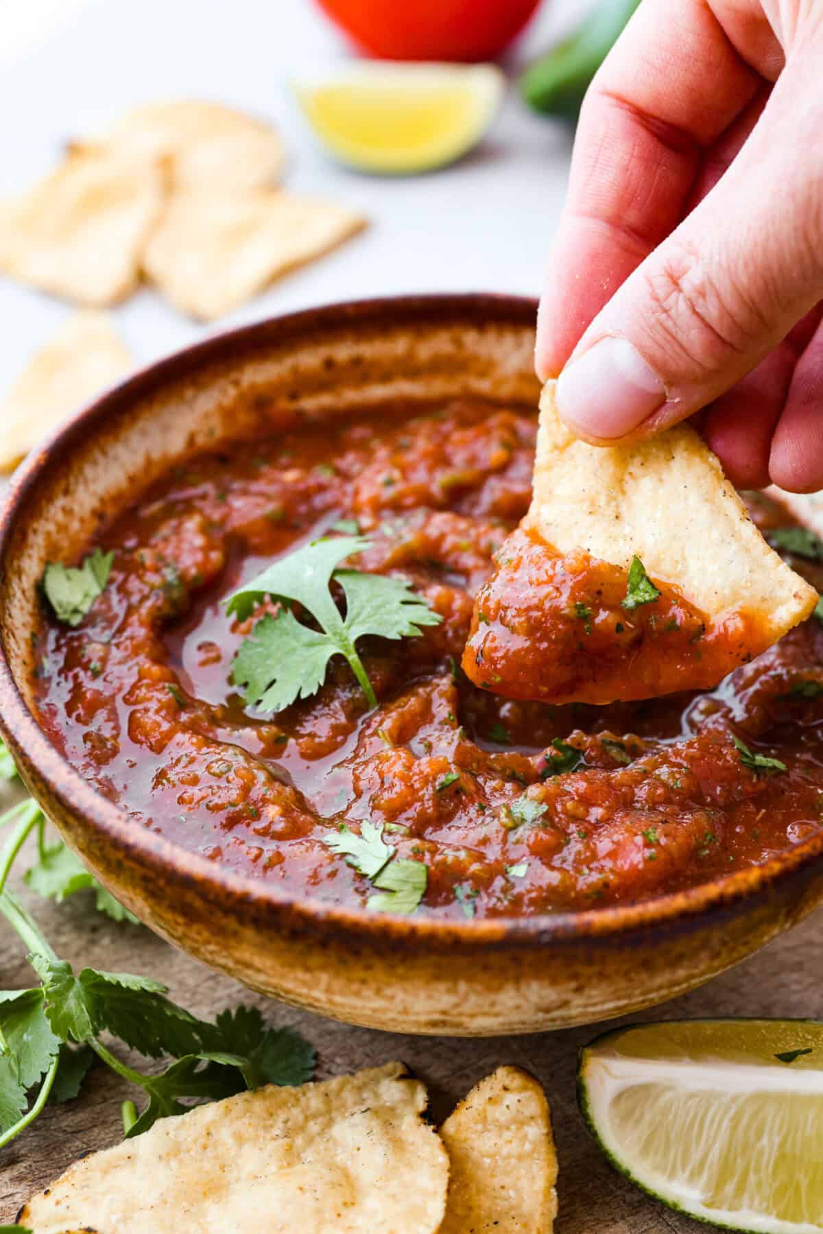 Close up shot of someone dipping a chip into bowl of salsa. 