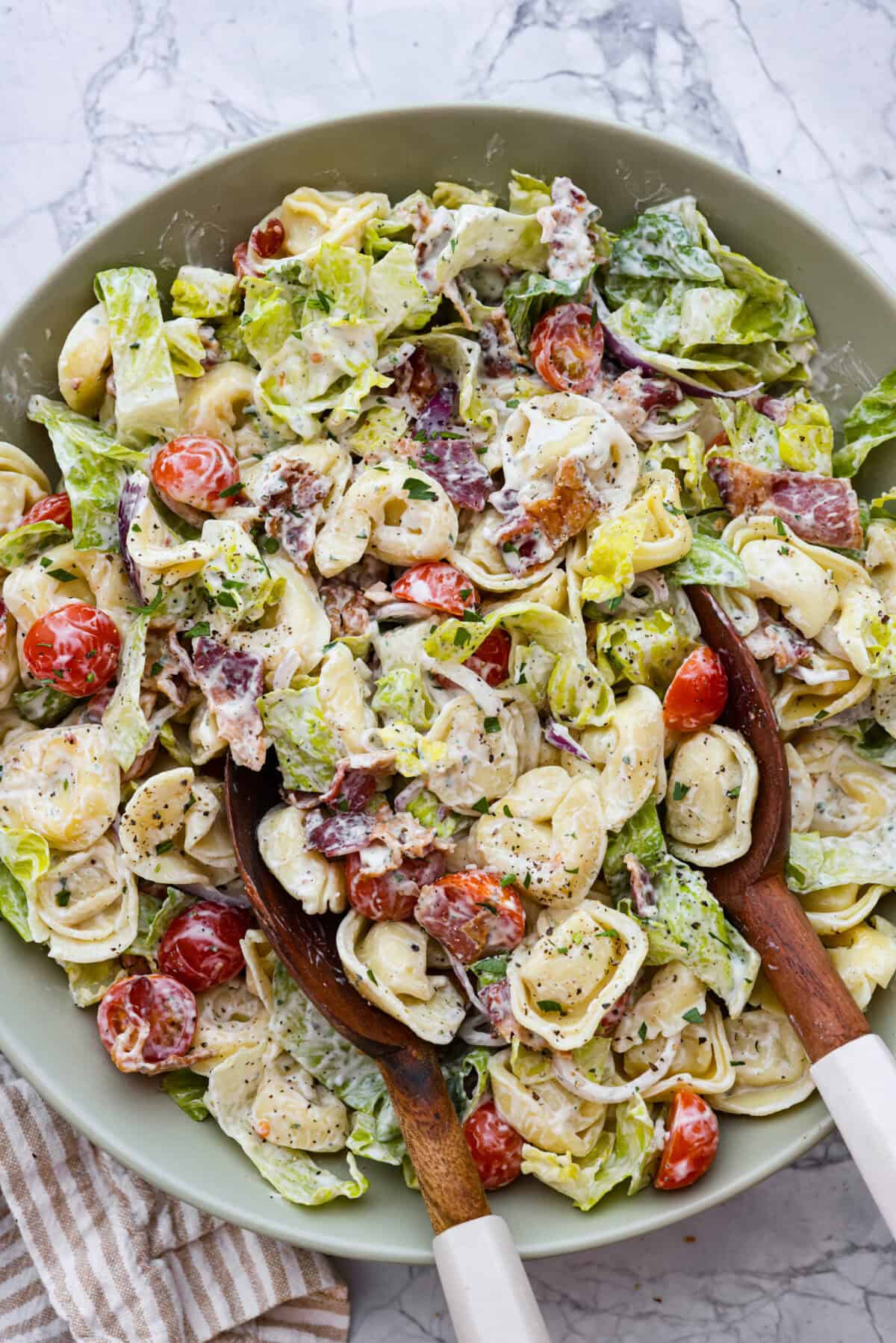 Overhead shot of BLT tortellini pasta salad in large bowl with wooden spoon. 