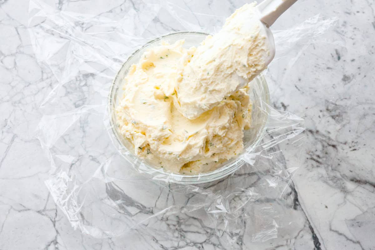 Boursin cheese is soft, creamy, and bursting with herbal flavor. Its texture is similar to cream cheese, making it incredibly versatile. It shines as a dip, enhances pasta dishes, complements meats, enriches sauces and soups, and so much more! Overhead shot of spatula putting scoops of mixed Boursin cheese ingredients into a bowl lined with saran wrap.