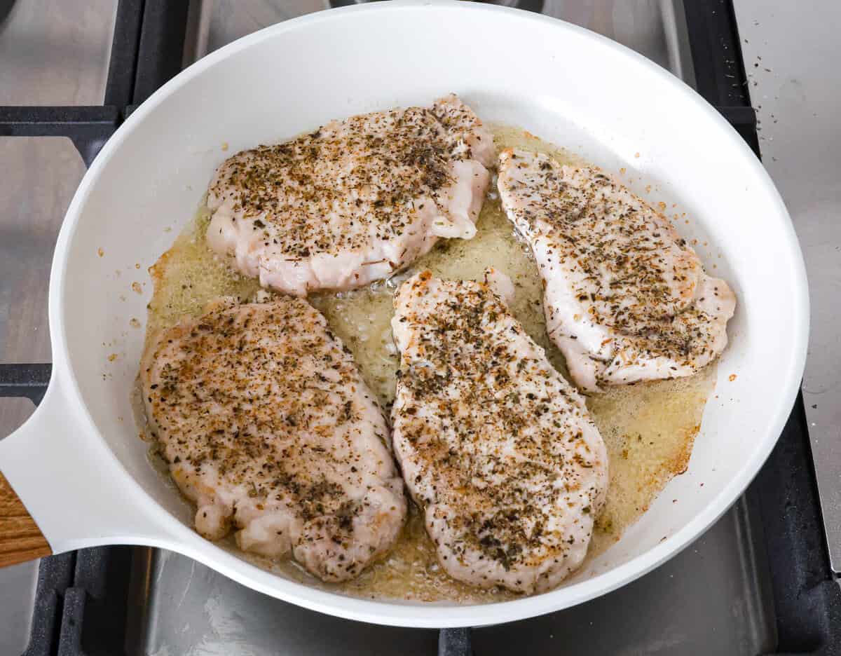 Boursin Pork Chops are savory, tender, and covered in a delicious cheesy cream sauce. This one-pan recipe is the perfect easy main that can be on your dinner table in just 30 minutes! Angle shot of seasoned pork chops in pan.