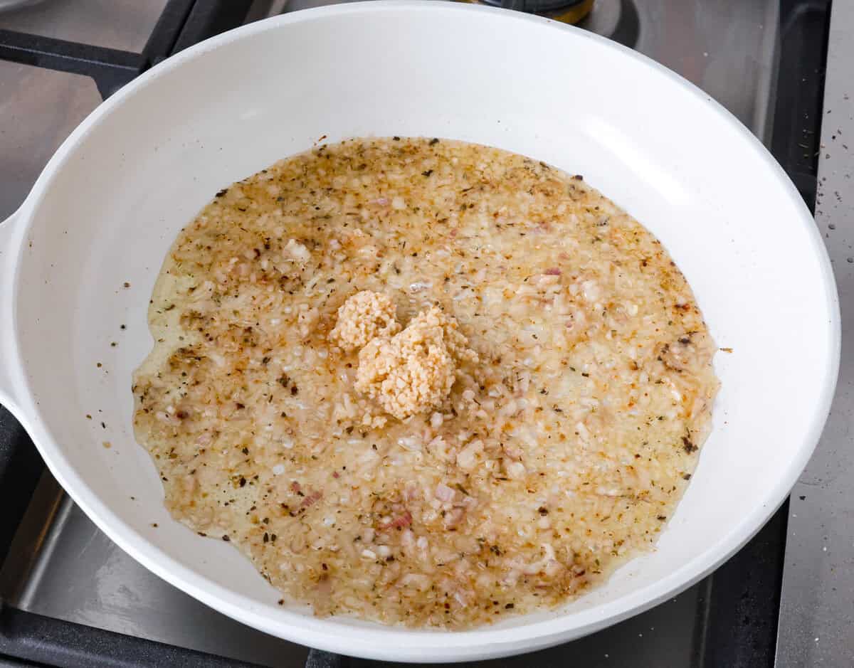 Boursin Pork Chops are savory, tender, and covered in a delicious cheesy cream sauce. This one-pan recipe is the perfect easy main that can be on your dinner table in just 30 minutes! Angle shot of garlic and shallots in sauce on pan.