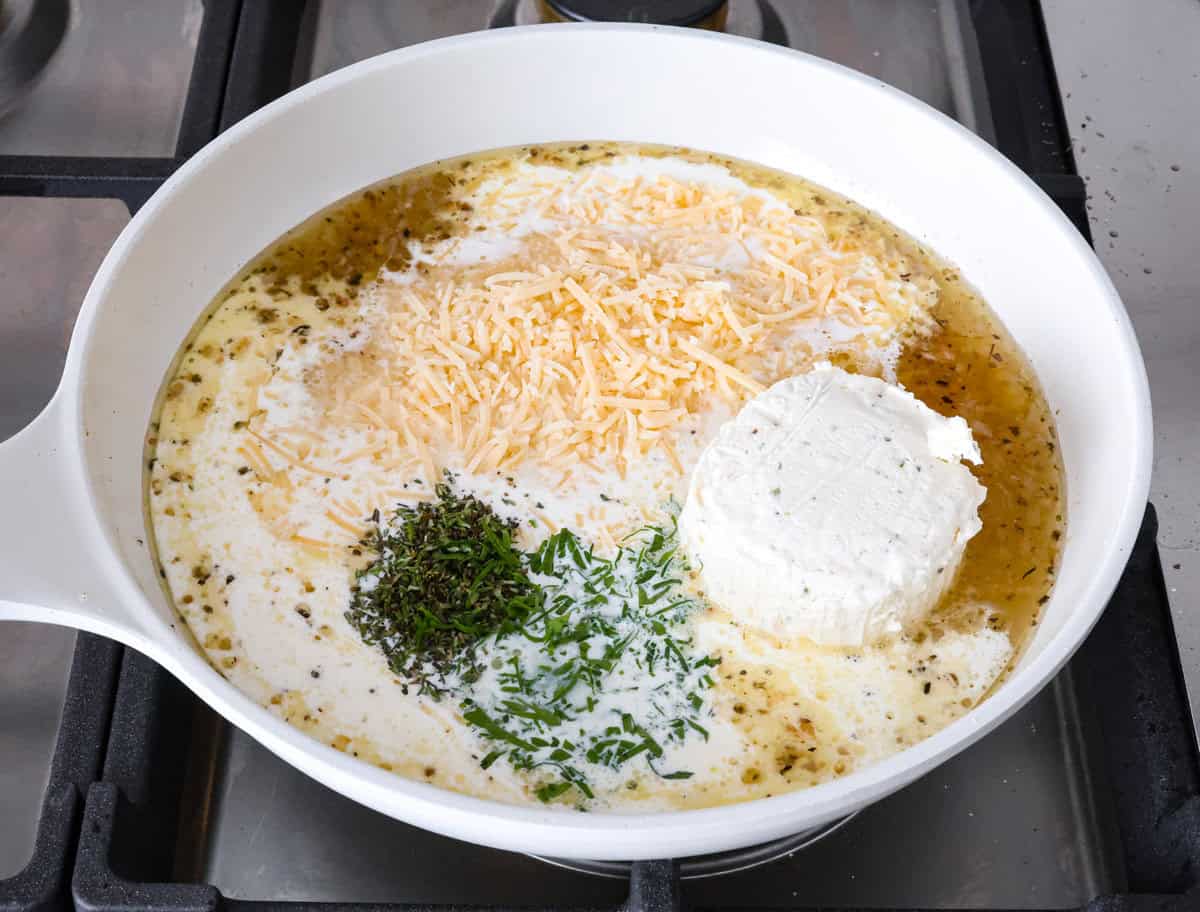 Boursin Pork Chops are savory, tender, and covered in a delicious cheesy cream sauce. This one-pan recipe is the perfect easy main that can be on your dinner table in just 30 minutes! Angle shot of cheese, herbs, and cream in sauce in pan.