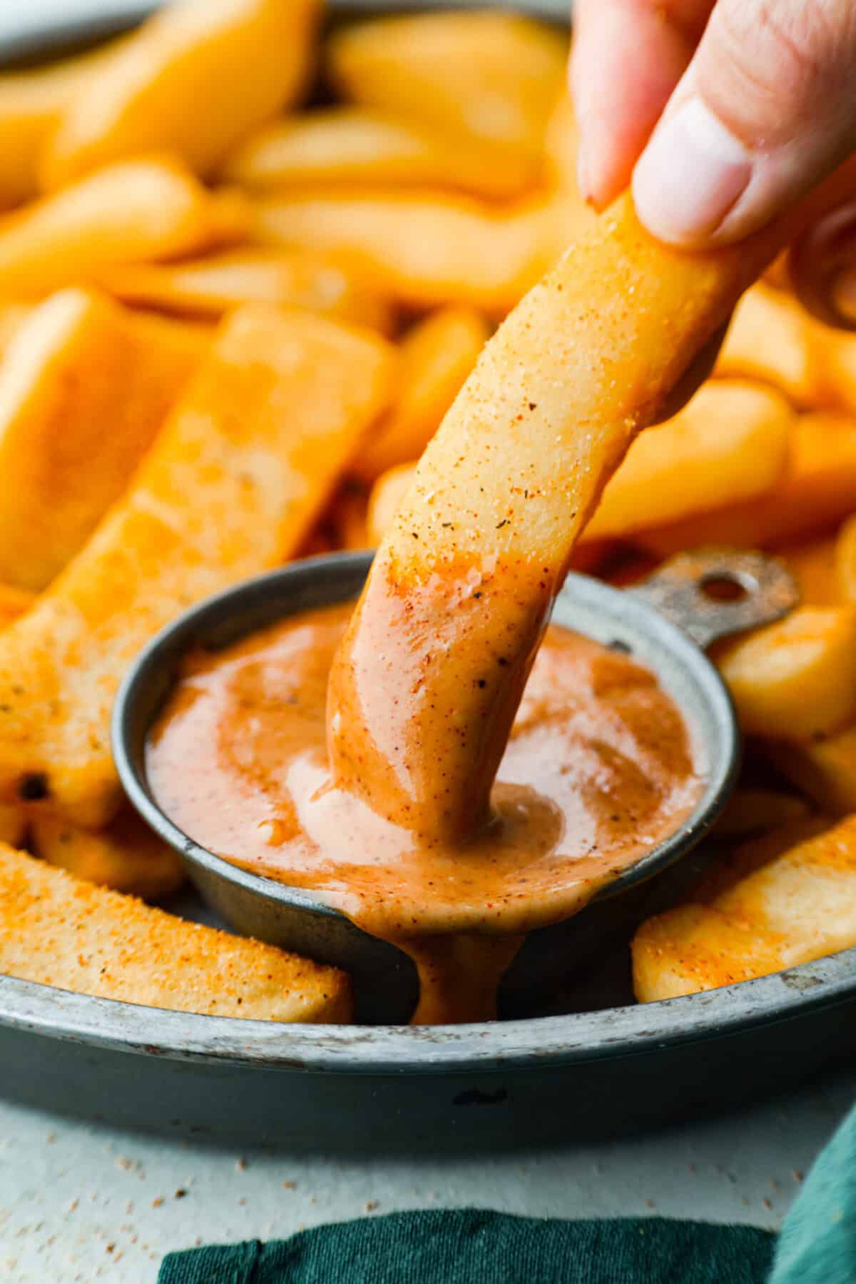 Close up shot of someone dipping a fry into a small bowl of re robin campfire sauce. 