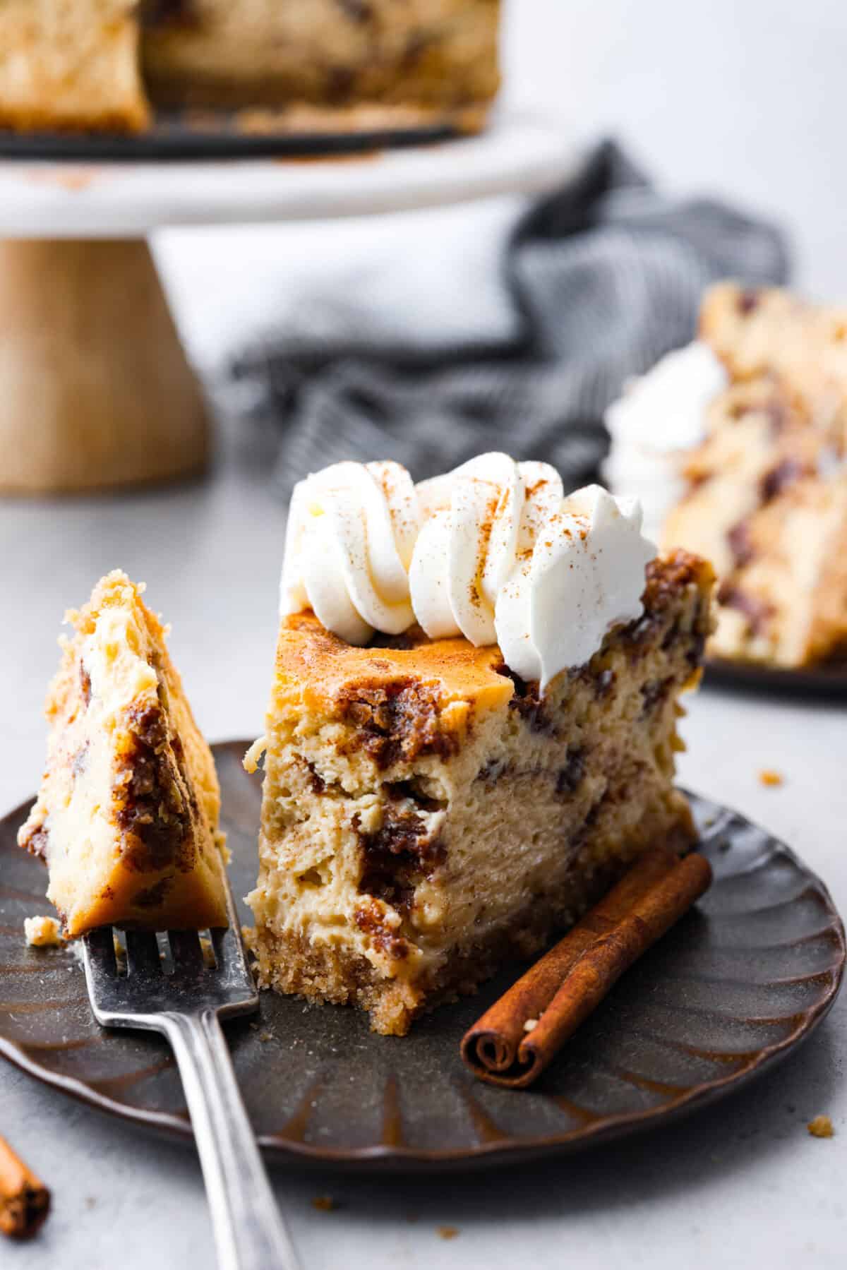 Side shot of plated slice of cinnamon roll cheesecake with a bit on a fork. 