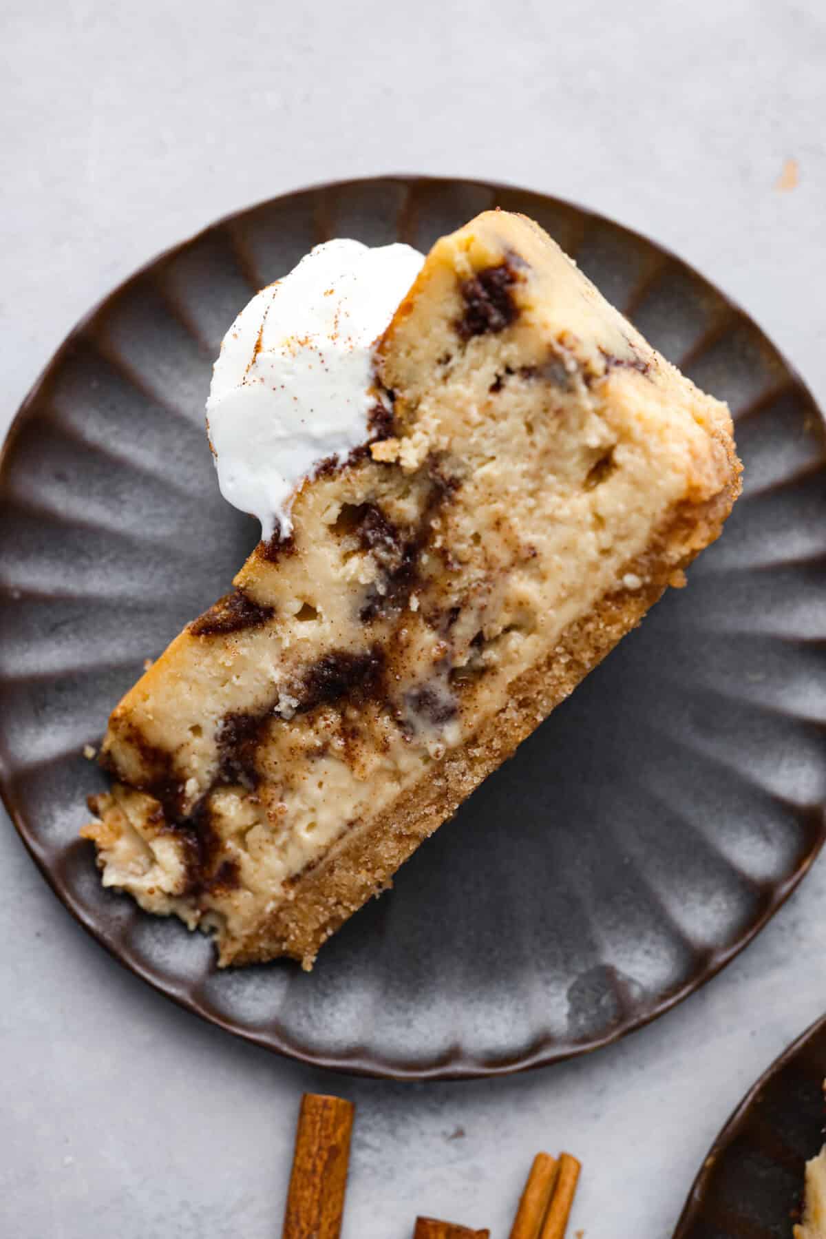 Overhead shot of a slice of cinnamon roll cheesecake on a plate tipped on its side. 