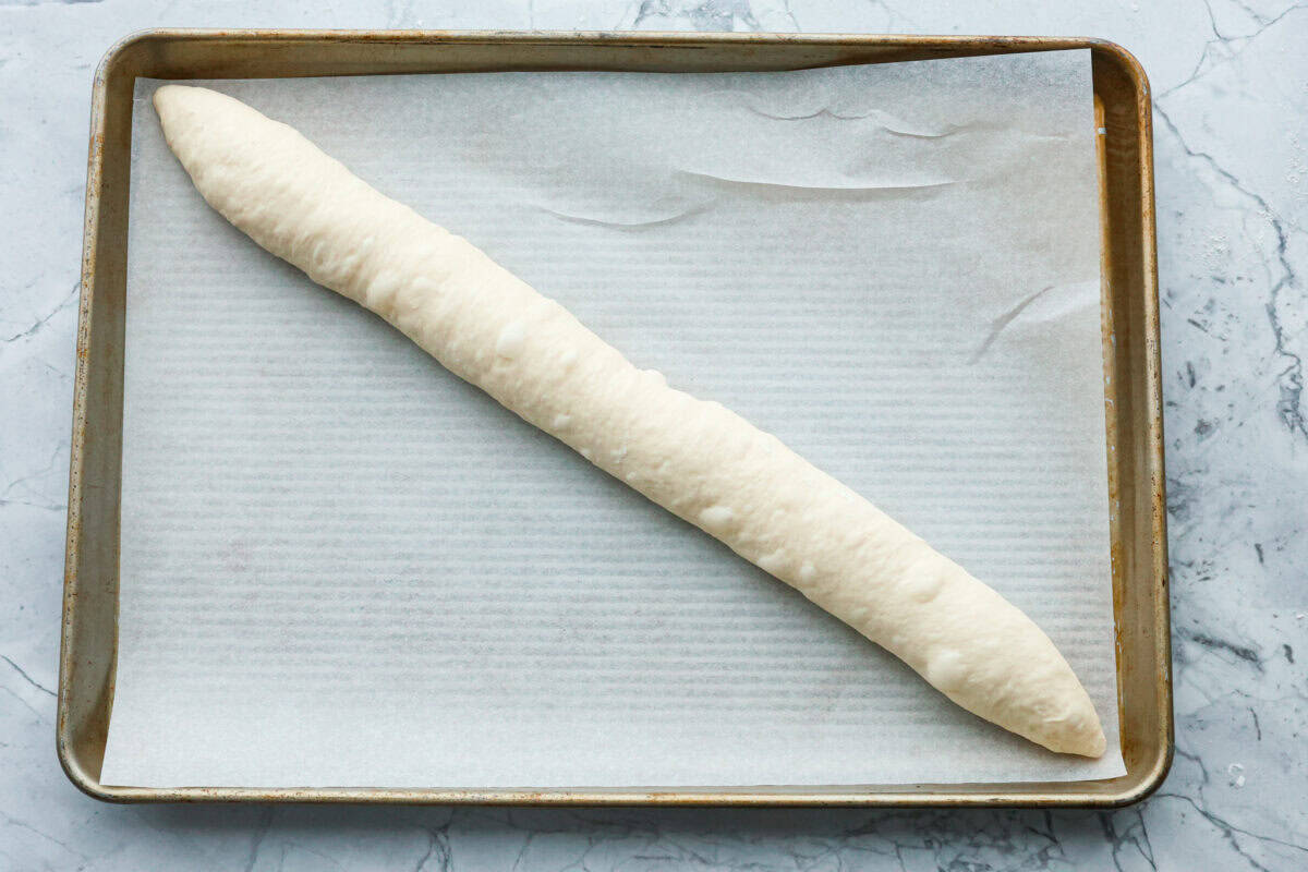 Overhead shot of French baguette dough at an angle on a parchment lined baking sheet. 