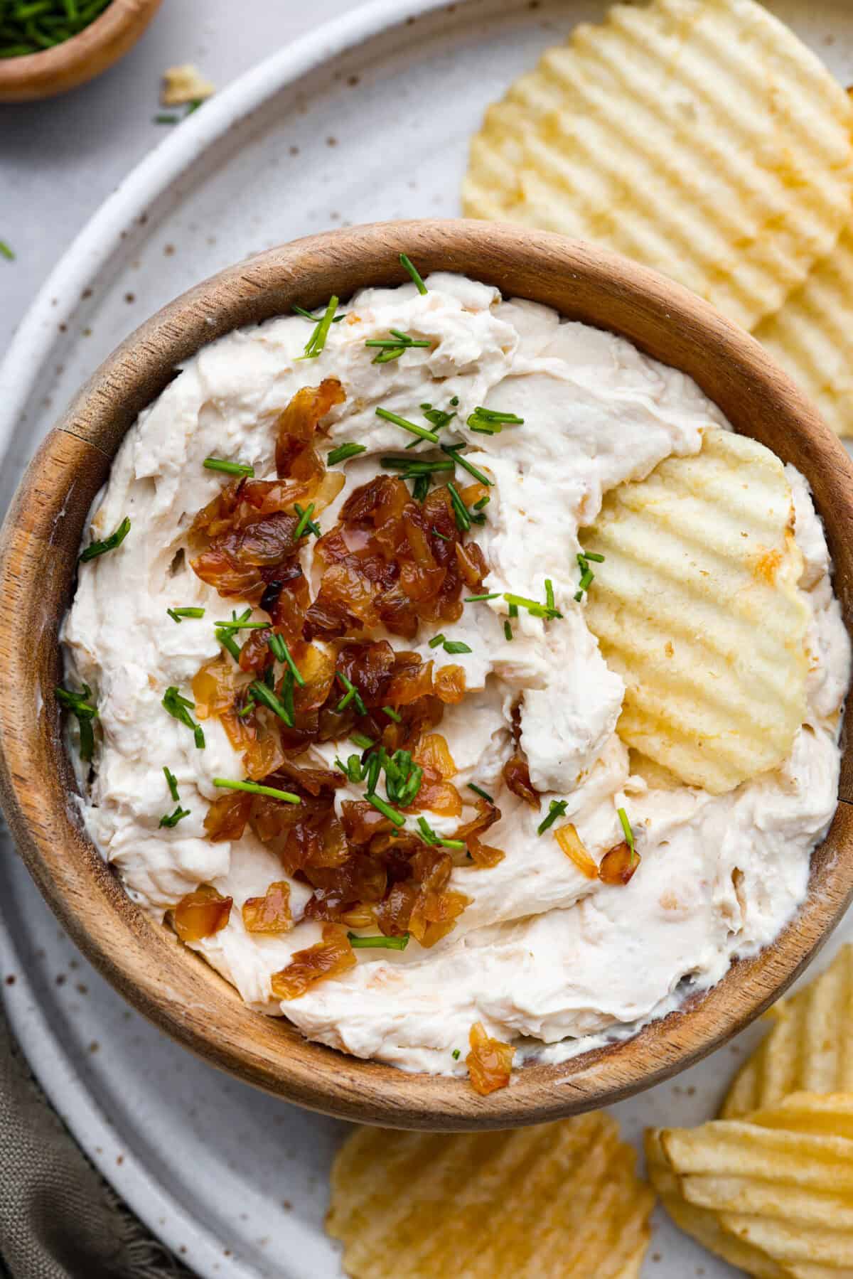 Top view of French onion dip garnished with caramelized onions and a chip on top.
