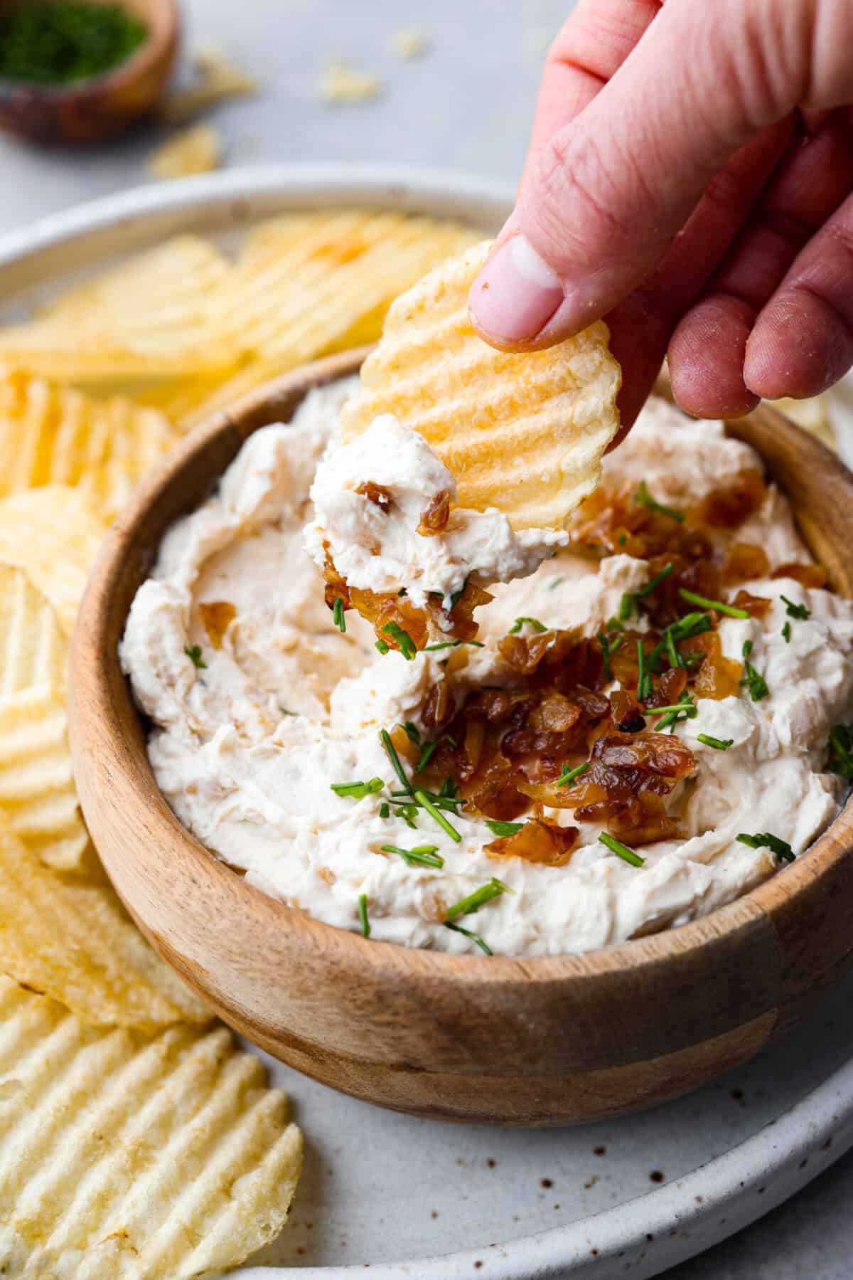 Close view of a chip dipping into bowl of French onion dip.