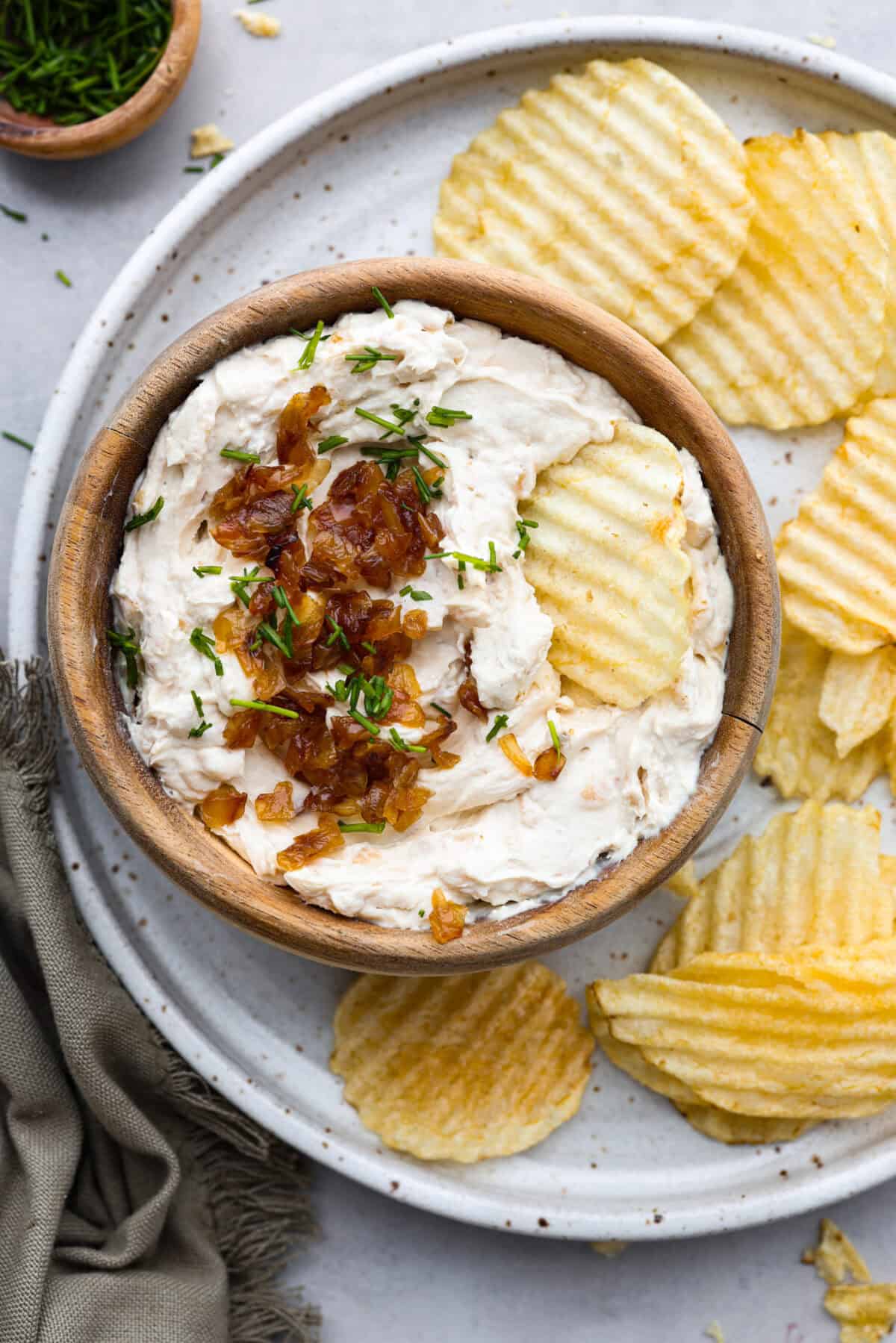 Top view of French onion dip in a wood bowl with chips on the side.