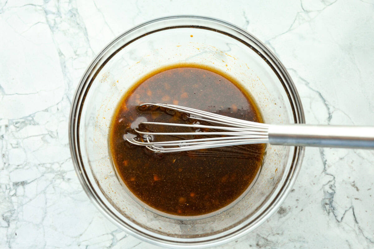 Overhead shot of marinade ingredients mixed in a bowl, with a whisk. 