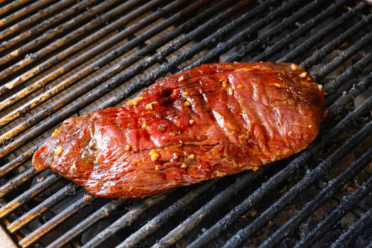 Angle shot of flank steak cooking on grill. 