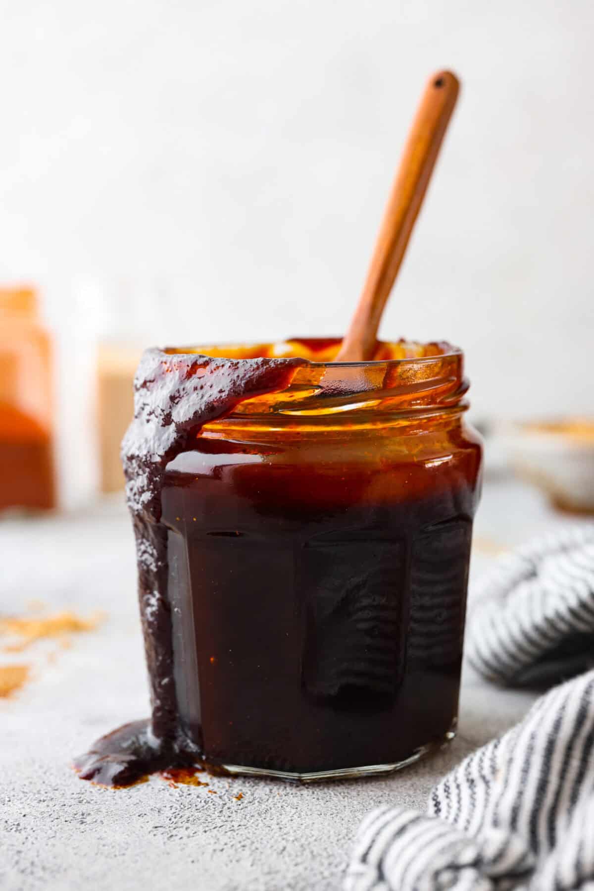Close view of a jar of bbq sauce with a wooden spoon and sauce drizzling down the side of the jar.