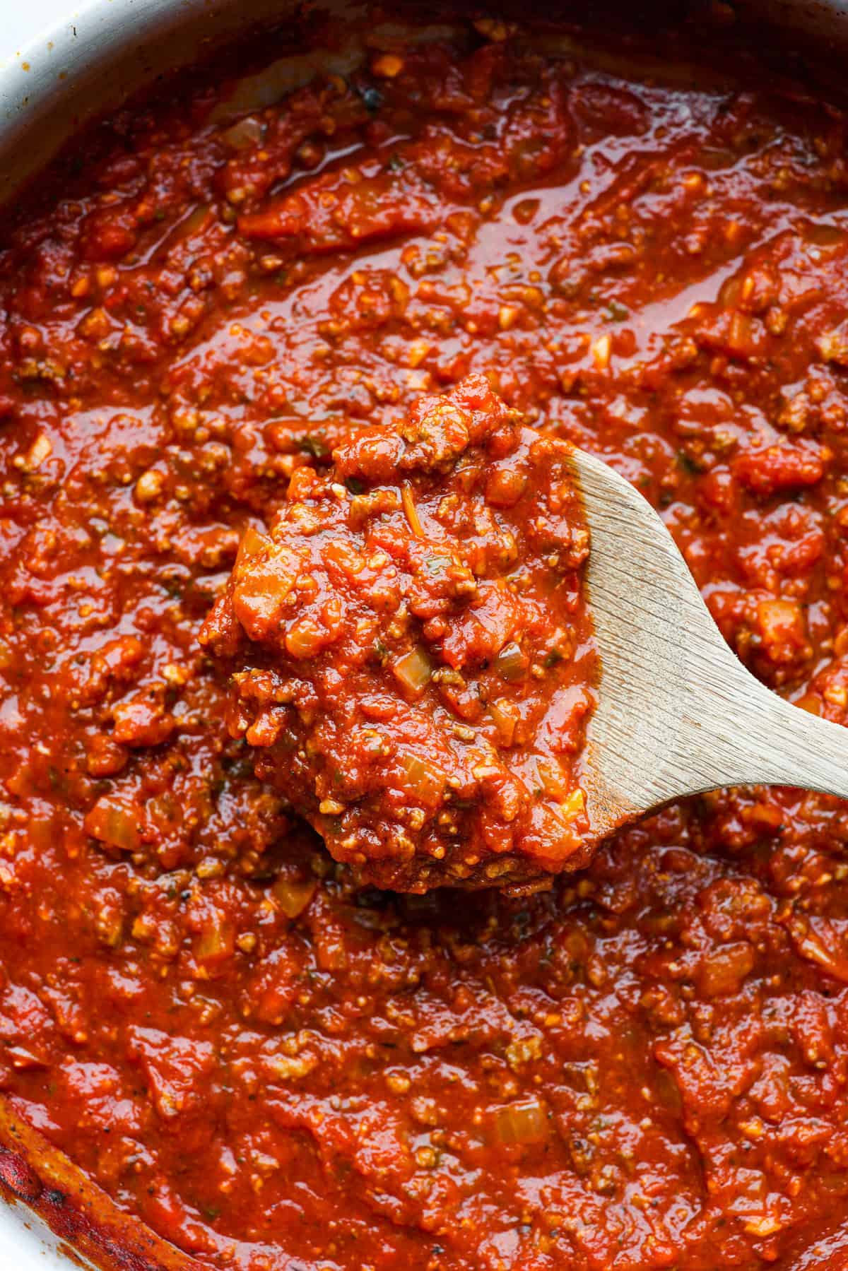 There's no need to purchase store-bought sauce, with this hearty and flavorful Homemade Spaghetti Sauce. Simple ingredients such as ground beef, onion, garlic, and spices of oregano and basil bring a bold flavor to this simple sauce. Close view of a wood spoon lifting up homemade spaghetti sauce.