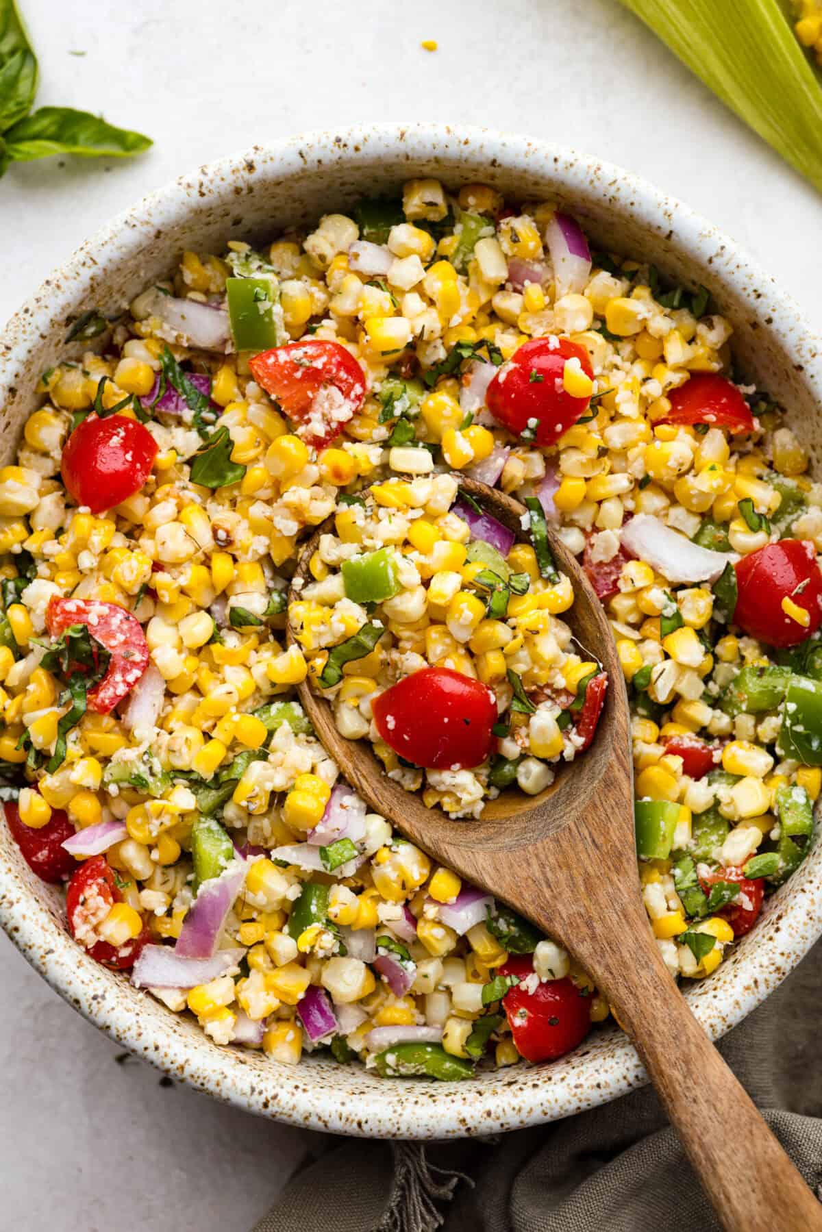 Overhead shot of Italian corn salad in bowl with wooden spoon. 