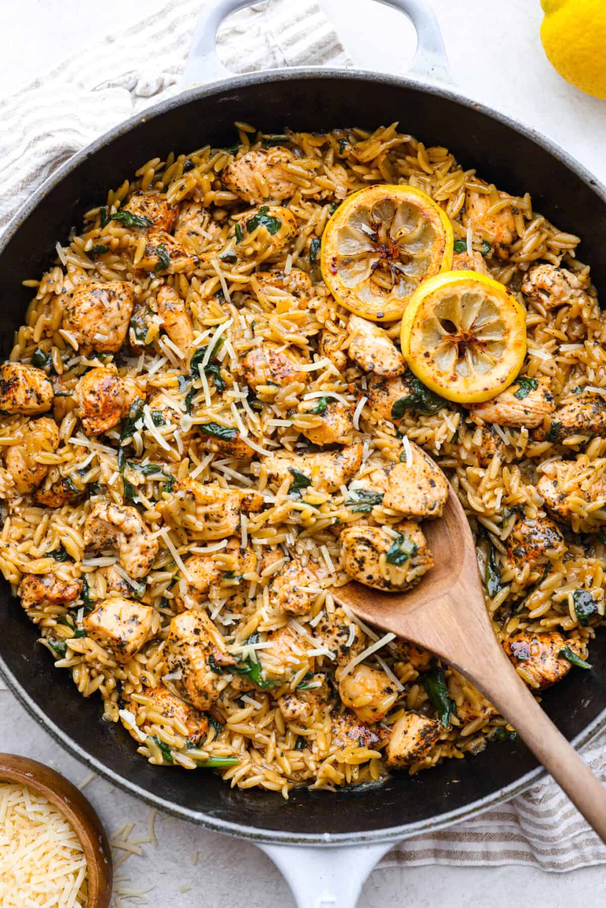 Overhead shot of one-pan lemon chicken orzo, with a wooden spoon and lemon slices as garnish. 