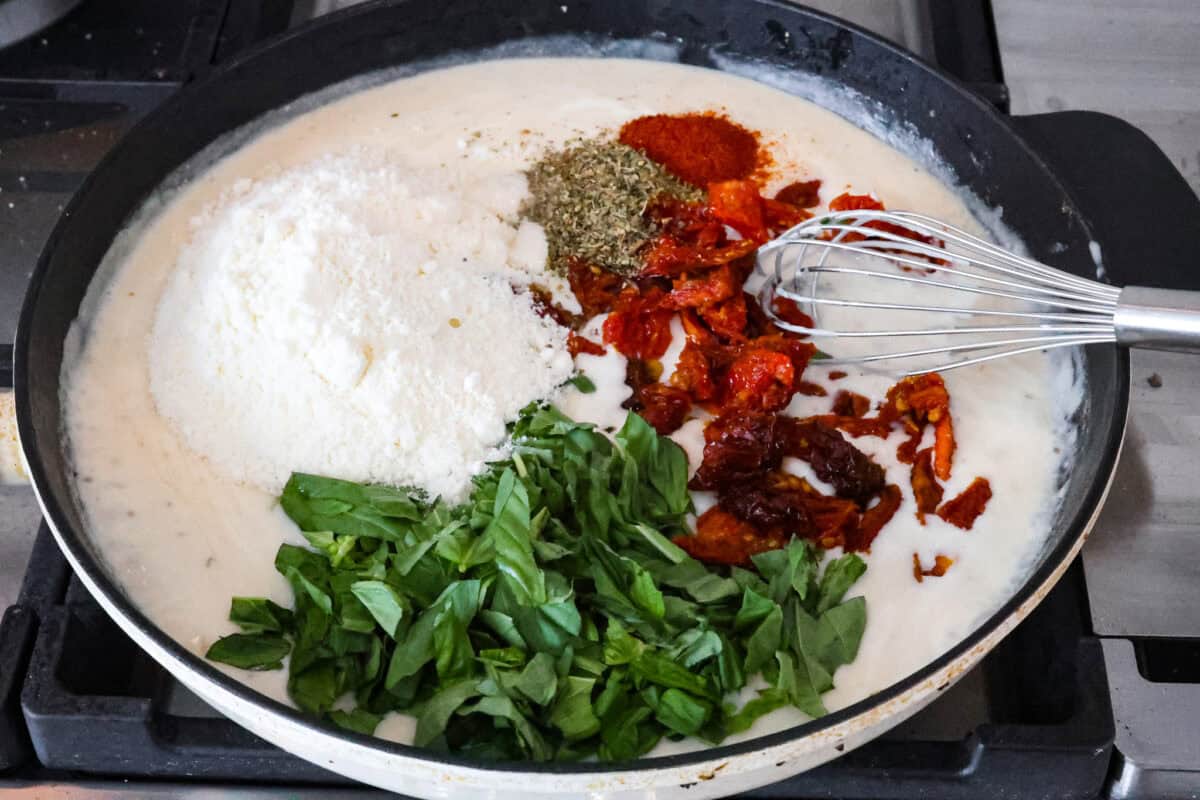 Angle shot of skillet with sauce, basil, sun-dried tomatoes, parmesan and seasonings. 