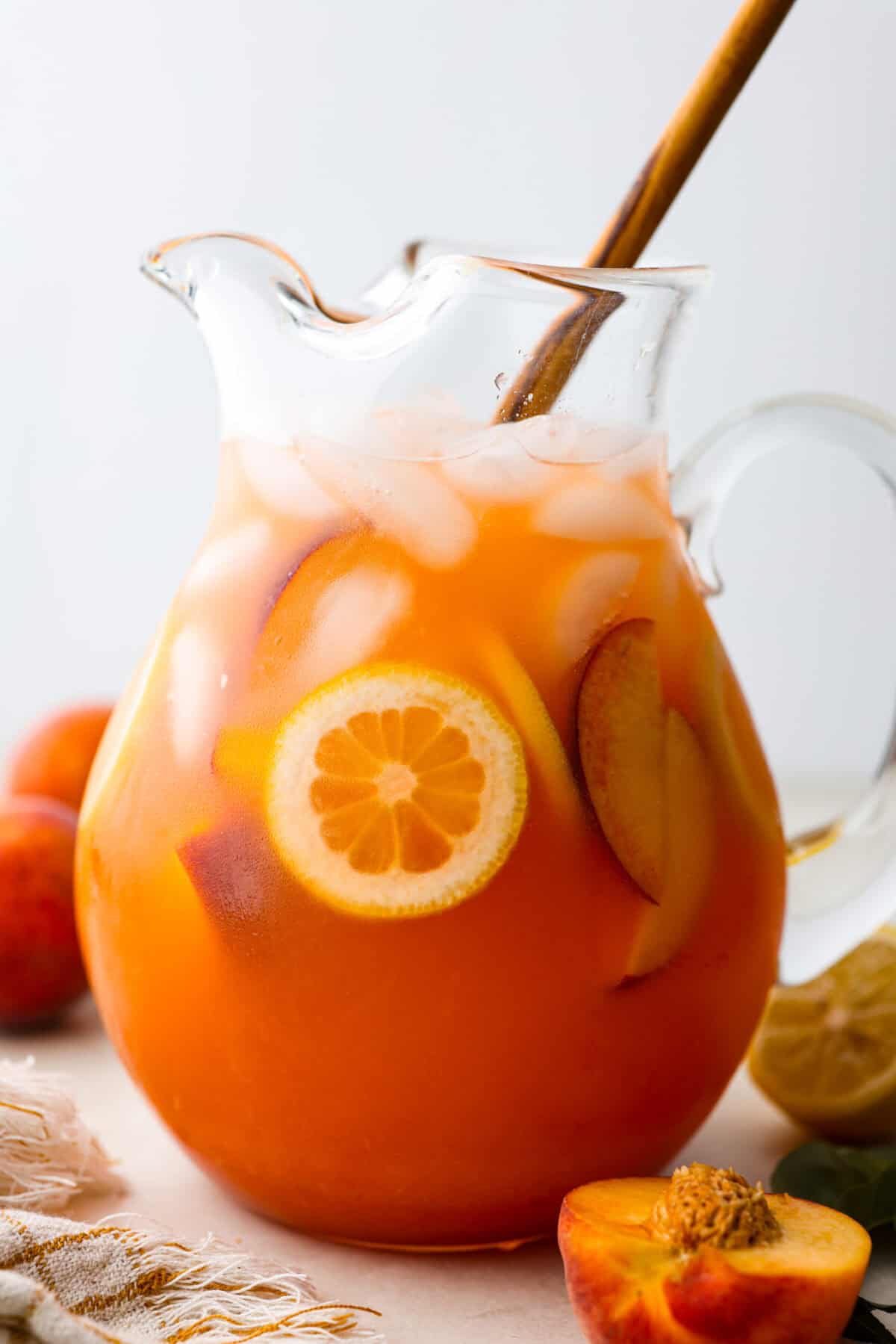 Side shot of Peach lemonade in a glass pitcher with a wooden spoon sticking.