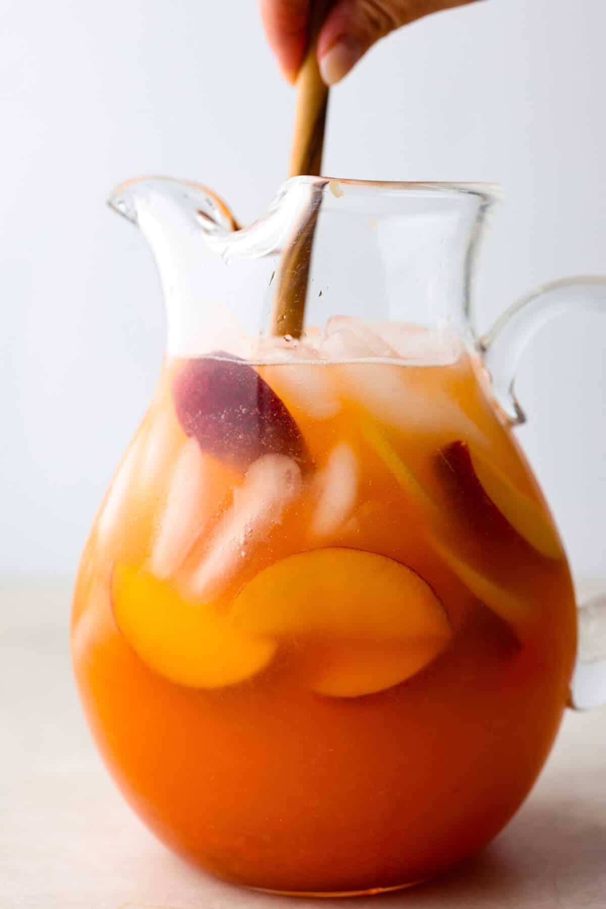 Side shot of pitcher of lemonade with someone stirring with a wooden spoon.