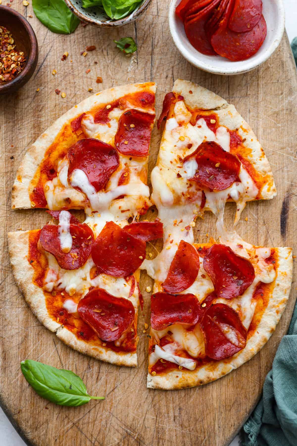 Overhead shot of sliced pita pizza on cutting board. 