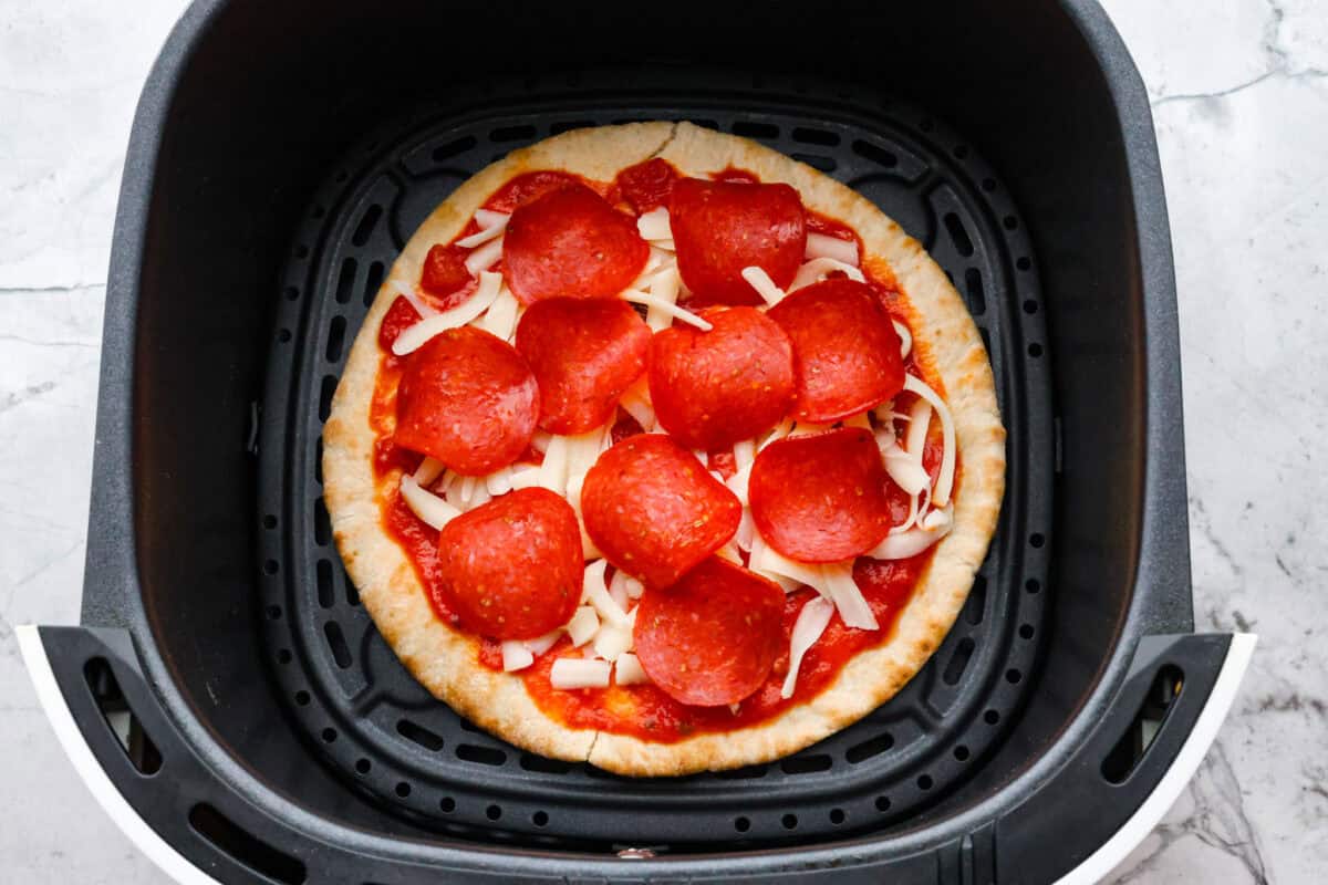 Overhead shot of pita pizza at the bottom of air fryer basket ready to be cooked. 