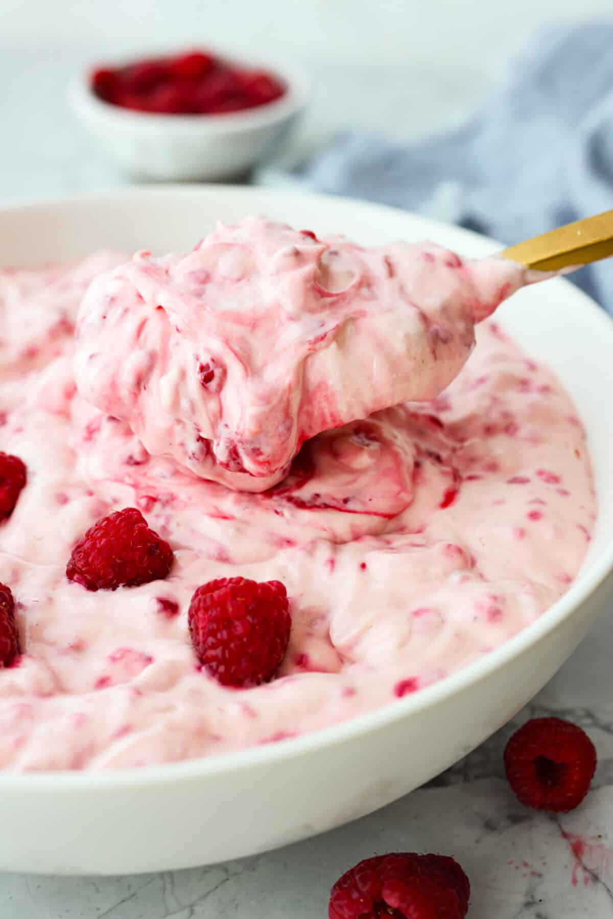 A close up side view of a scoop of raspberry fluff salad with a gold spoon. 