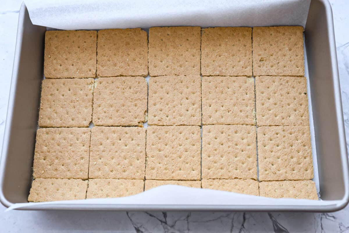 Overhead shot of a pan with a layer of parchment covered in a single layer of graham crackers. 