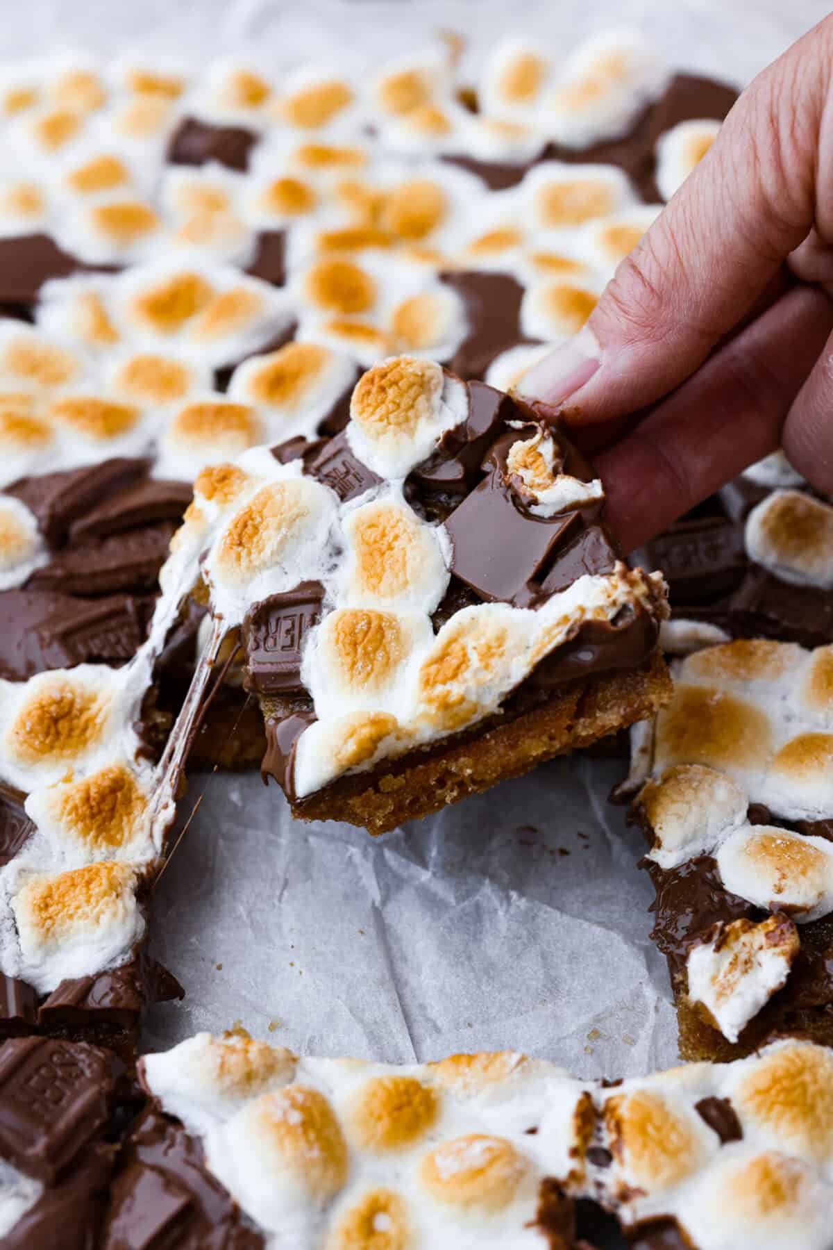 Angled zoomed in shot of someone pulling a piece of gooey s'mores crack from the pan.