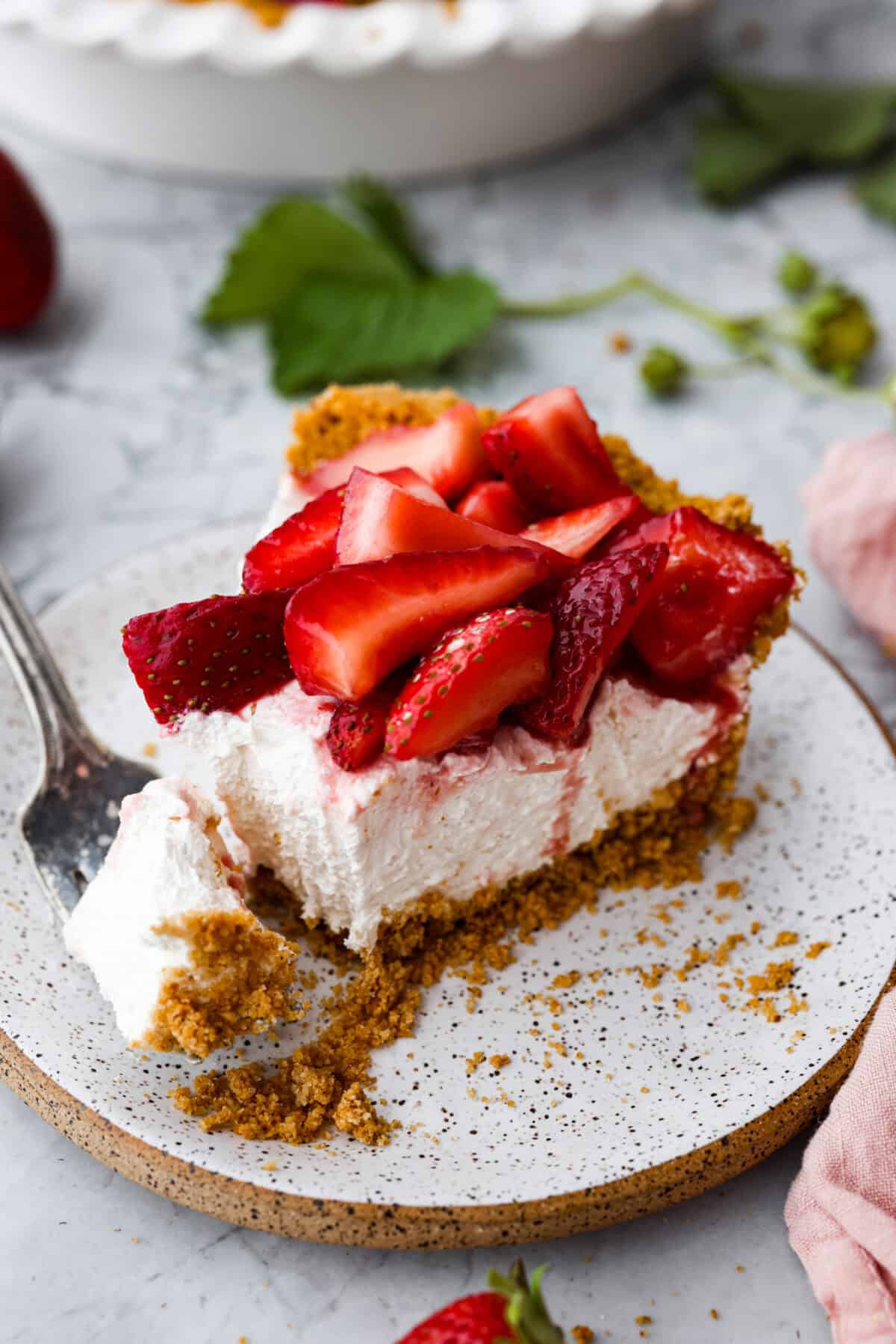 Angle shot of a slice of strawberry cream pie on a plate with a bite taken out on a fork next to it. 
