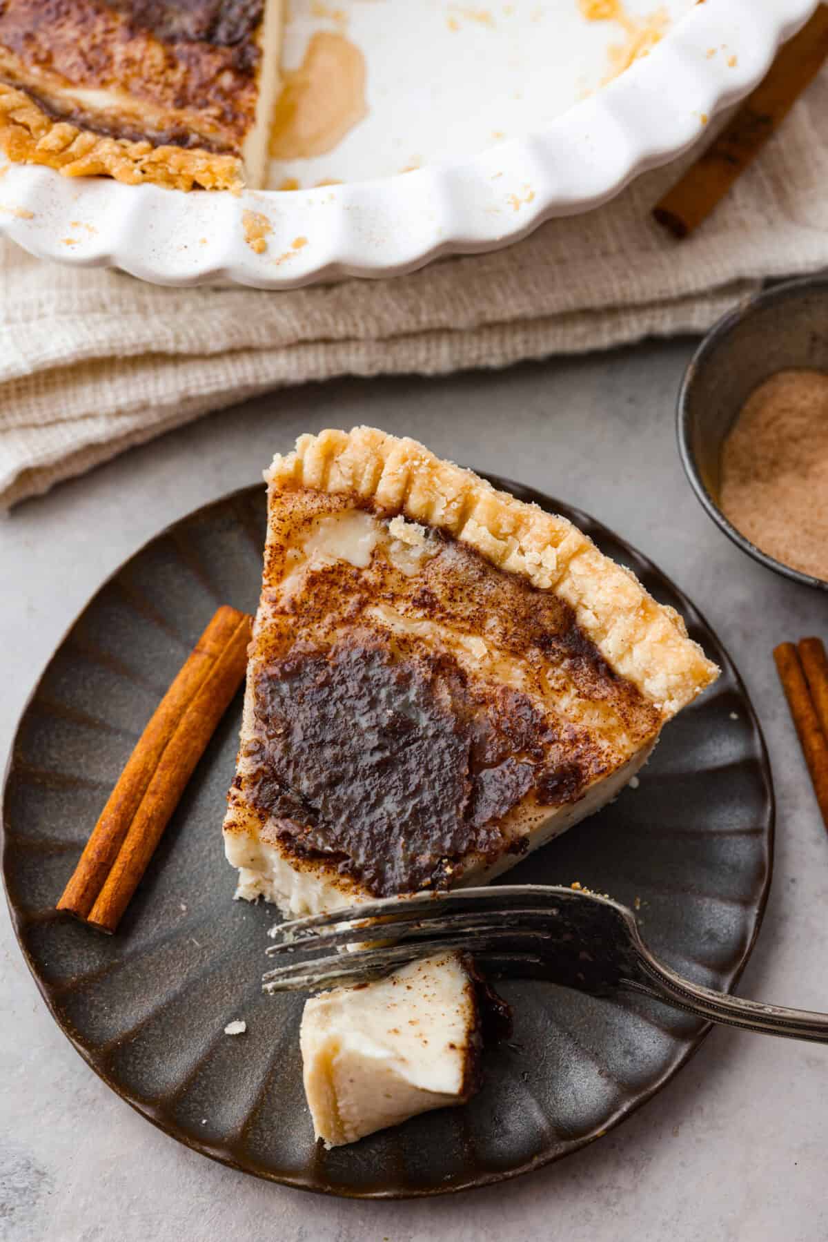 Overhead shot of a slice of sugar cream pie plated with a fork and a bite cut out of it. 