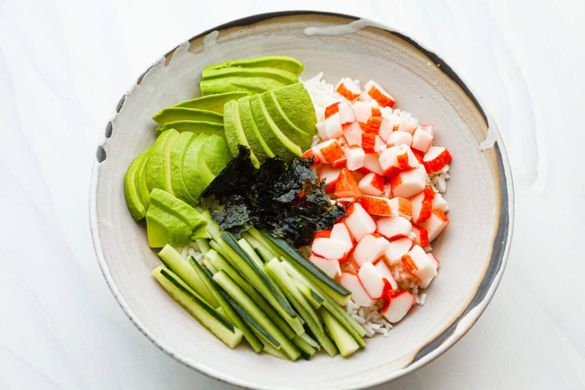 Overhead shot of bowl with rice, crab, avocado, cucumber and seaweed. 