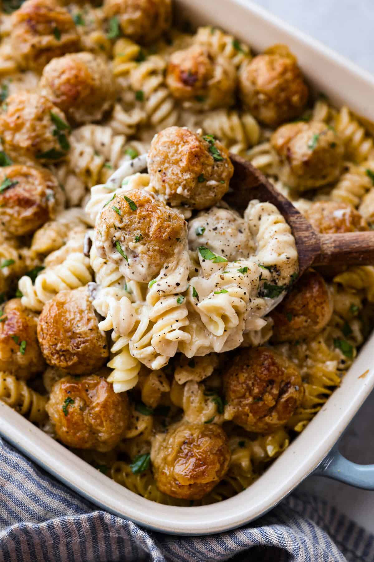 Swedish Meatball Casserole is a classic comfort meal the whole family will enjoy! Tender meatballs are layered over perfectly cooked pasta and baked in a rich, creamy gravy. This dinner recipe is easy enough to make during the week but also deliciously impressive for entertaining! Close up shot of a wooden spoon with a scoop of Swedish meatball casserole.