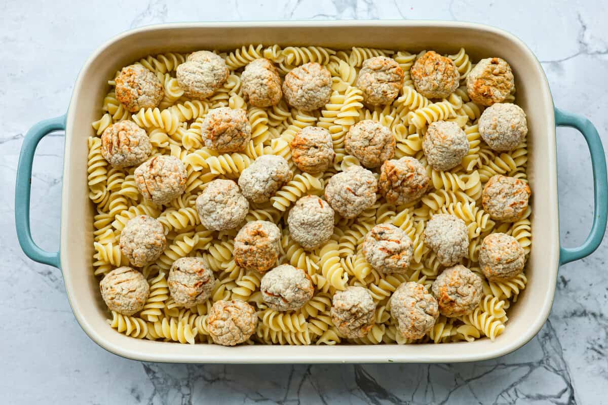 Swedish Meatball Casserole is a classic comfort meal the whole family will enjoy! Tender meatballs are layered over perfectly cooked pasta and baked in a rich, creamy gravy. This dinner recipe is easy enough to make during the week but also deliciously impressive for entertaining! Overhead shot of casserole dish with pasta on the bottom with meatballs spaced out on top.