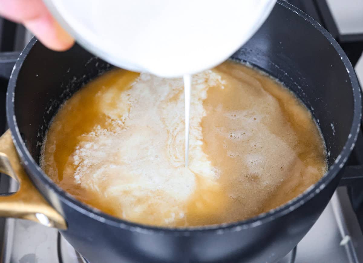 Swedish Meatball Casserole is a classic comfort meal the whole family will enjoy! Tender meatballs are layered over perfectly cooked pasta and baked in a rich, creamy gravy. This dinner recipe is easy enough to make during the week but also deliciously impressive for entertaining! Overhead shot of someone pouring cream into the gravy mixture.
