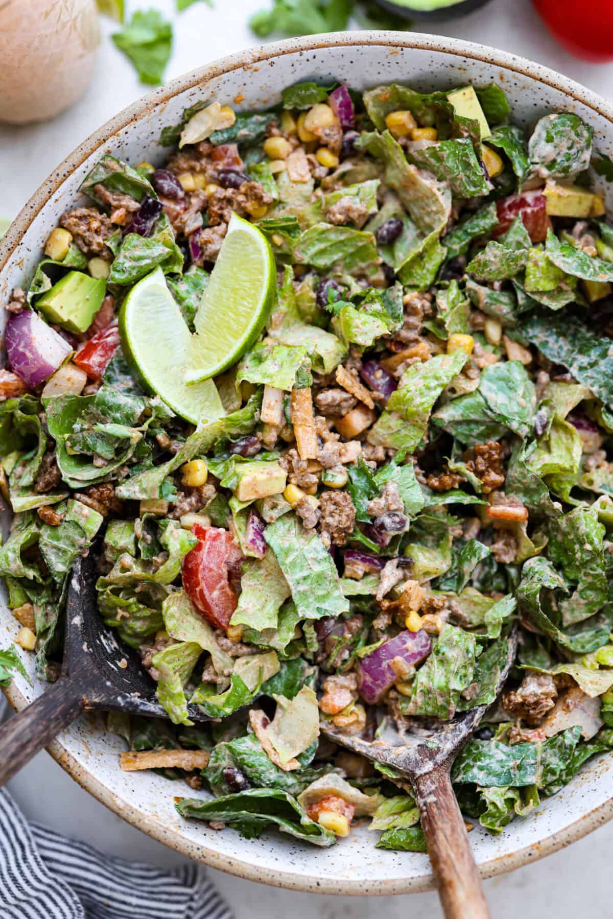 Overhead shot of completed beef taco salad in large bowl, with limes wedges on top. 