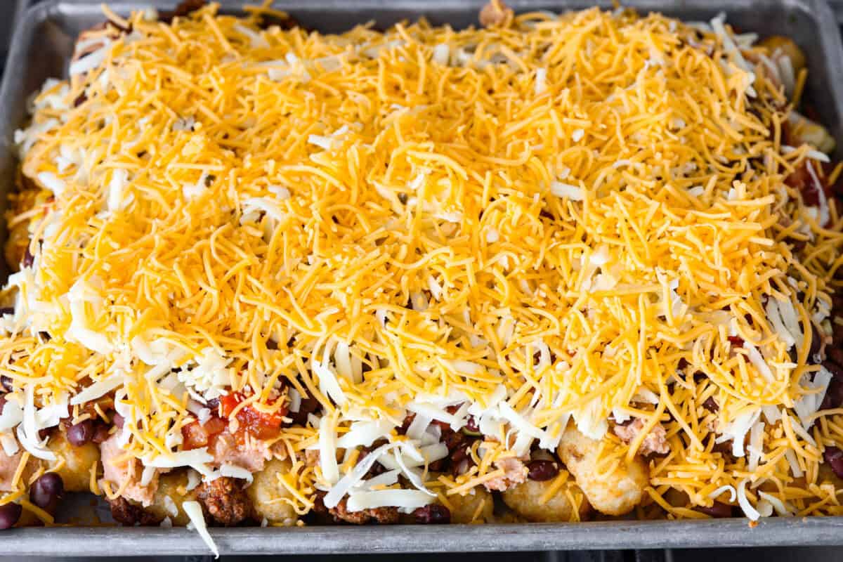 Overhead shot of prepared pan of tater tot nachos with shredded cheese over the top. 