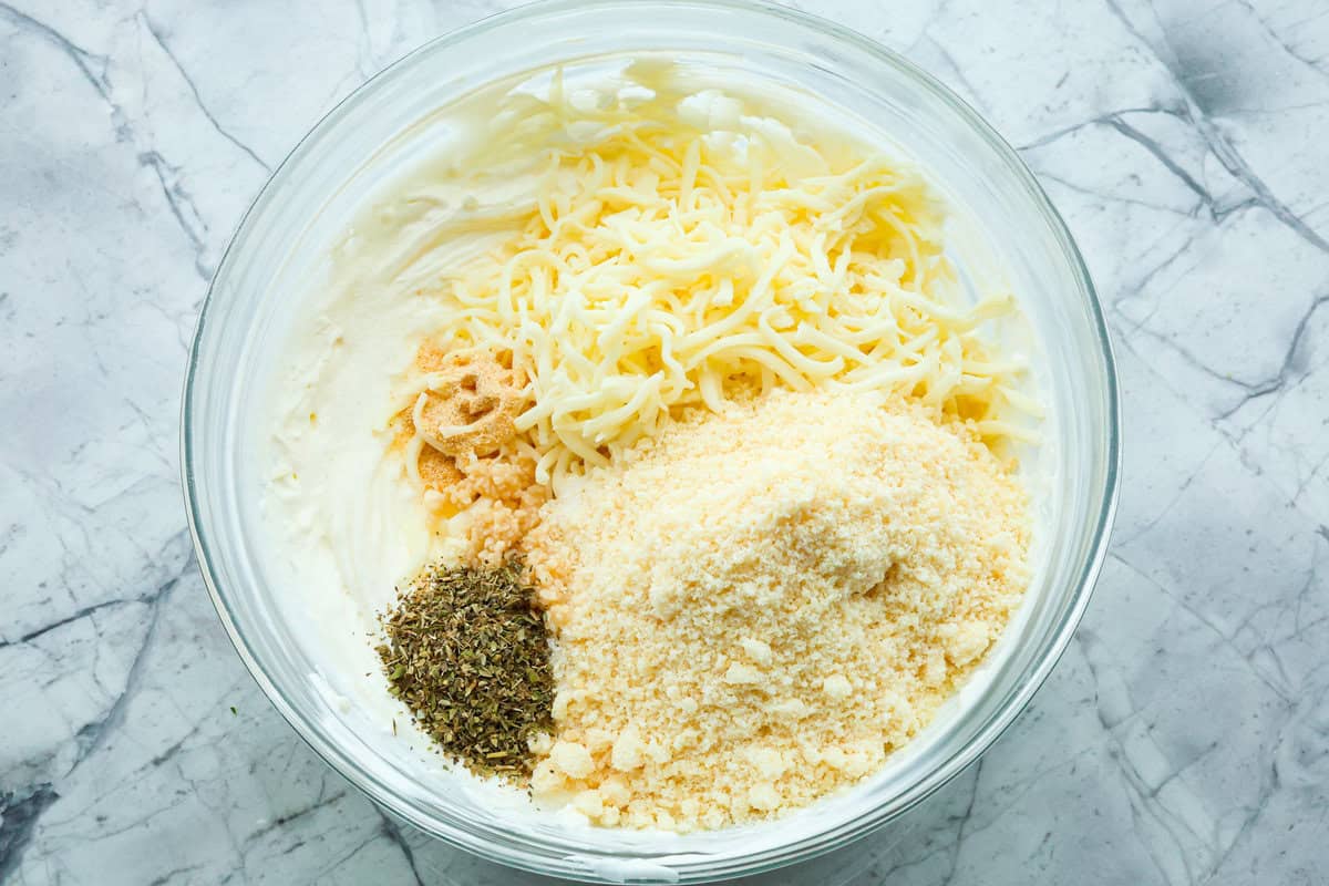 There's a new appetizer in town, and this creamy Tuscan dip won everyone's hearts! The combination of cheeses, garlic, spinach, and sun-dried tomatoes creates an addicting dip you’ll want to bring to all of your gatherings! Second photo of the seasonings and cheeses added to the bowl.