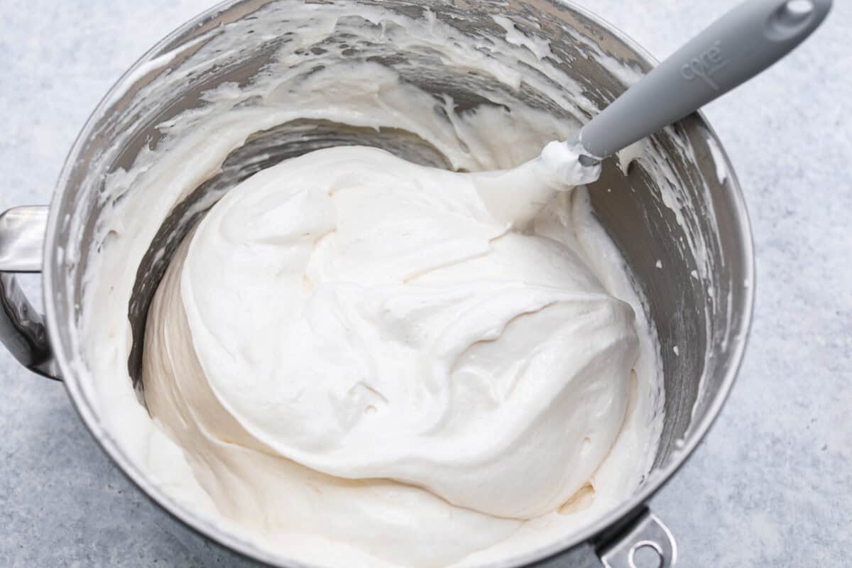 Overhead shot of bowl of egg whites with a spatula folding in flour. 